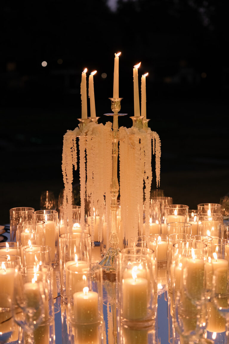 A tall candelabra with trailing pale amaranthus surrounded by glass hurricane candles at night, IAMFLOWER