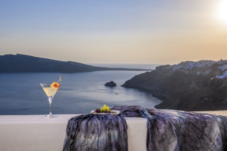A cocktail on a terrace wall at sunset above the caldera, Ikies Traditional Houses