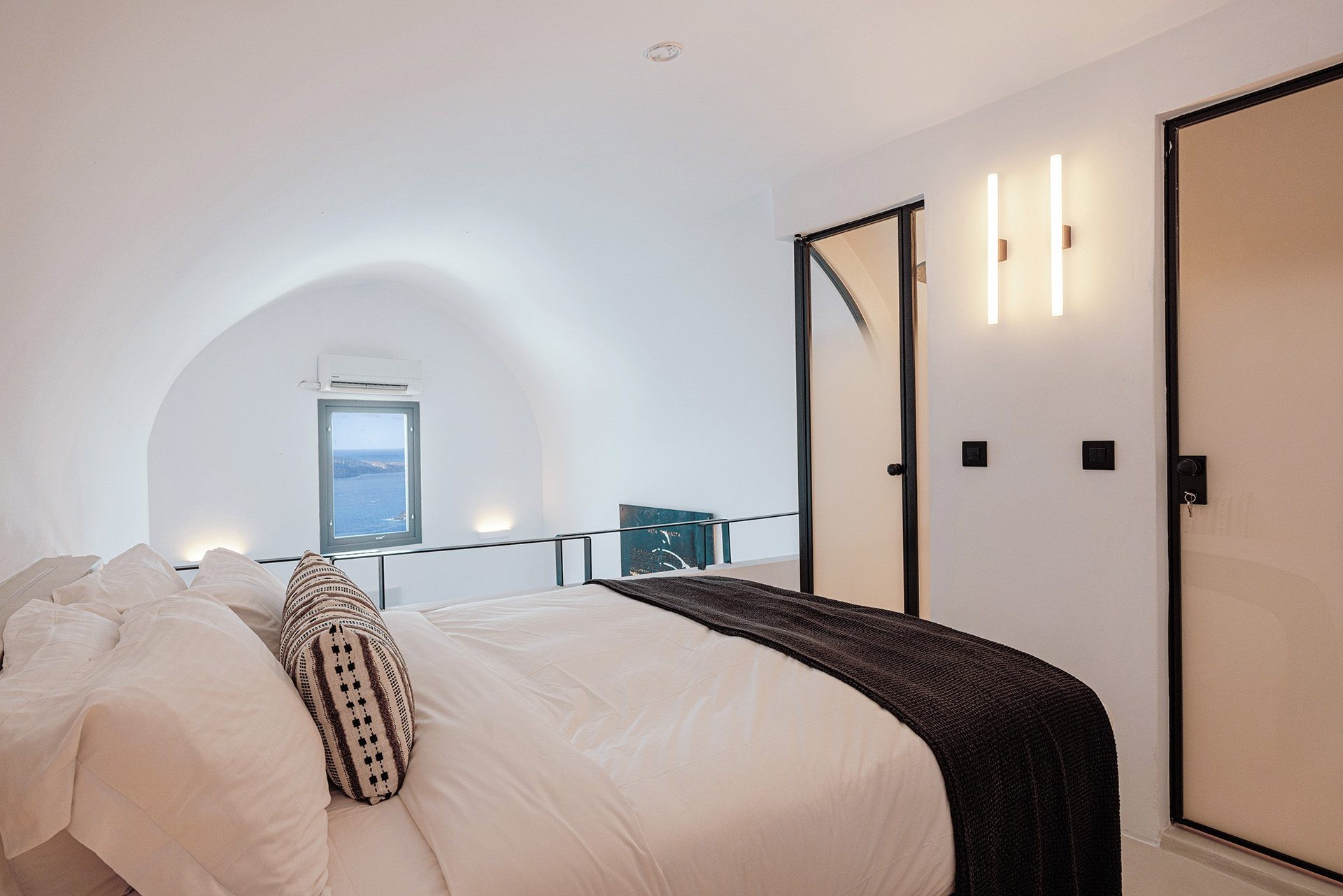 A bed on a raised level of white plaster, a metal rail and a tall window above the living space