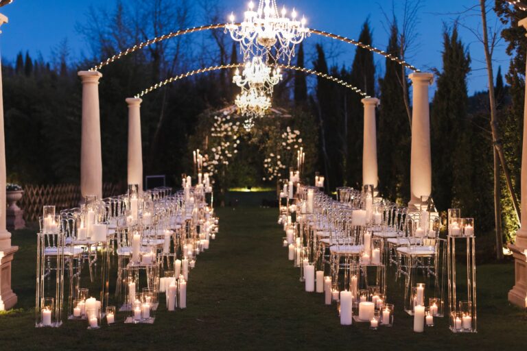 An evening ceremony aisle in a Tuscan garden: white columns, strings of lights, crystal chandeliers and hundreds of candles on glass stands, Il Giorno Perfetto di Glenda Marradi