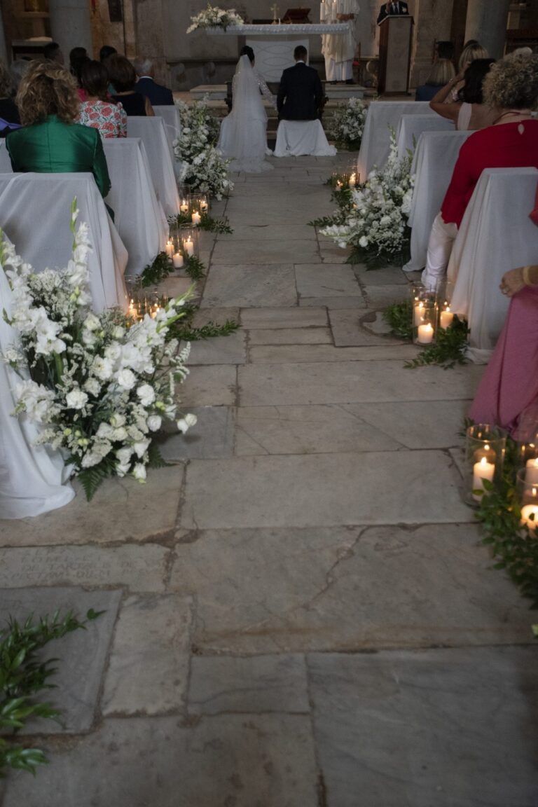 A stone church aisle lined with white flowers and pillar candles, Il Giorno Perfetto di Glenda Marradi
