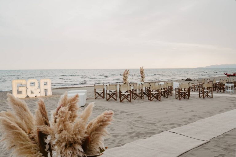 A beach ceremony set up with director's chairs, pampas grass and lit initials by the sea, Il Giorno Perfetto di Glenda Marradi