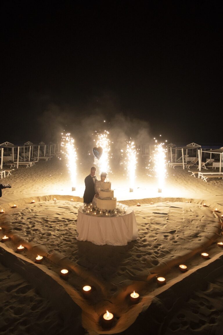 The wedding cake inside a heart of candles on the sand, sparkler fountains behind, Il Giorno Perfetto di Glenda Marradi