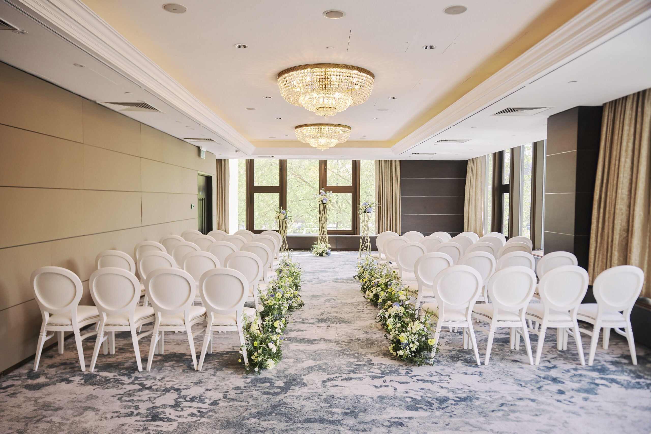 White chairs either side of a flower-lined aisle in one of the event suites, with tall windows onto trees outside, InterContinental London Park Lane