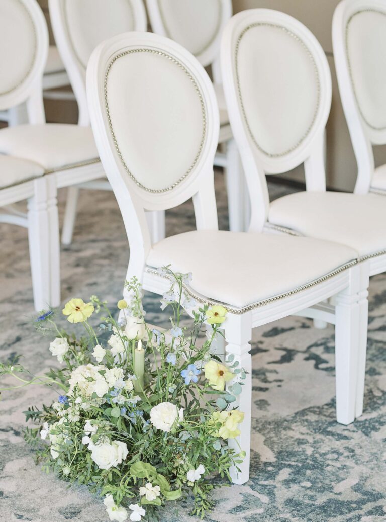 Upholstered white ceremony chairs with loose meadow-style flowers placed along the aisle, InterContinental London Park Lane