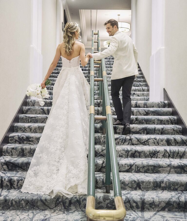 A bride and groom climbing a carpeted staircase with a brass-capped handrail inside the hotel, InterContinental London Park Lane