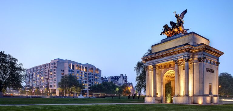The hotel's long facade at dusk seen across Hyde Park Corner, with the floodlit Wellington Arch and its bronze quadriga in the foreground, InterContinental London Park Lane