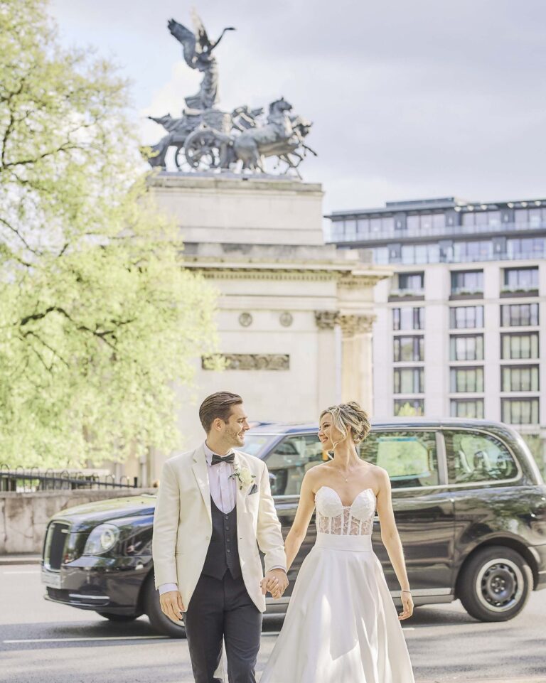 A bride and groom walking hand in hand past a black London taxi, with the Wellington Arch quadriga and the hotel behind them, InterContinental London Park Lane
