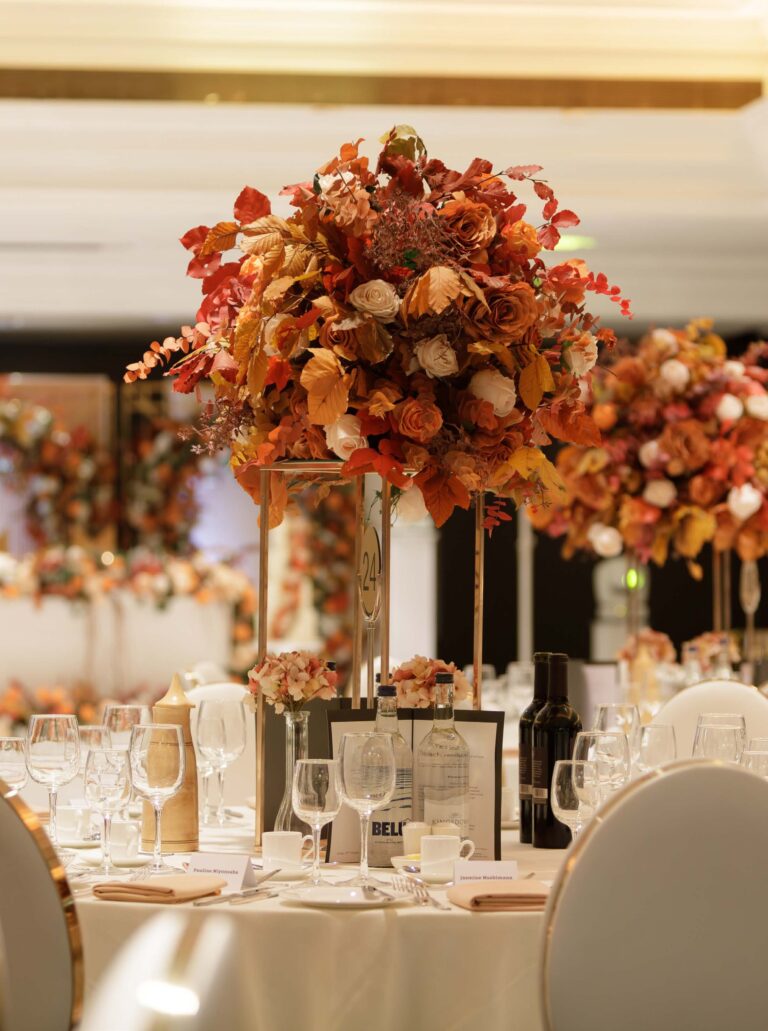 Round tables in the Ballroom under tall arrangements of copper and orange autumn foliage and roses, InterContinental London Park Lane