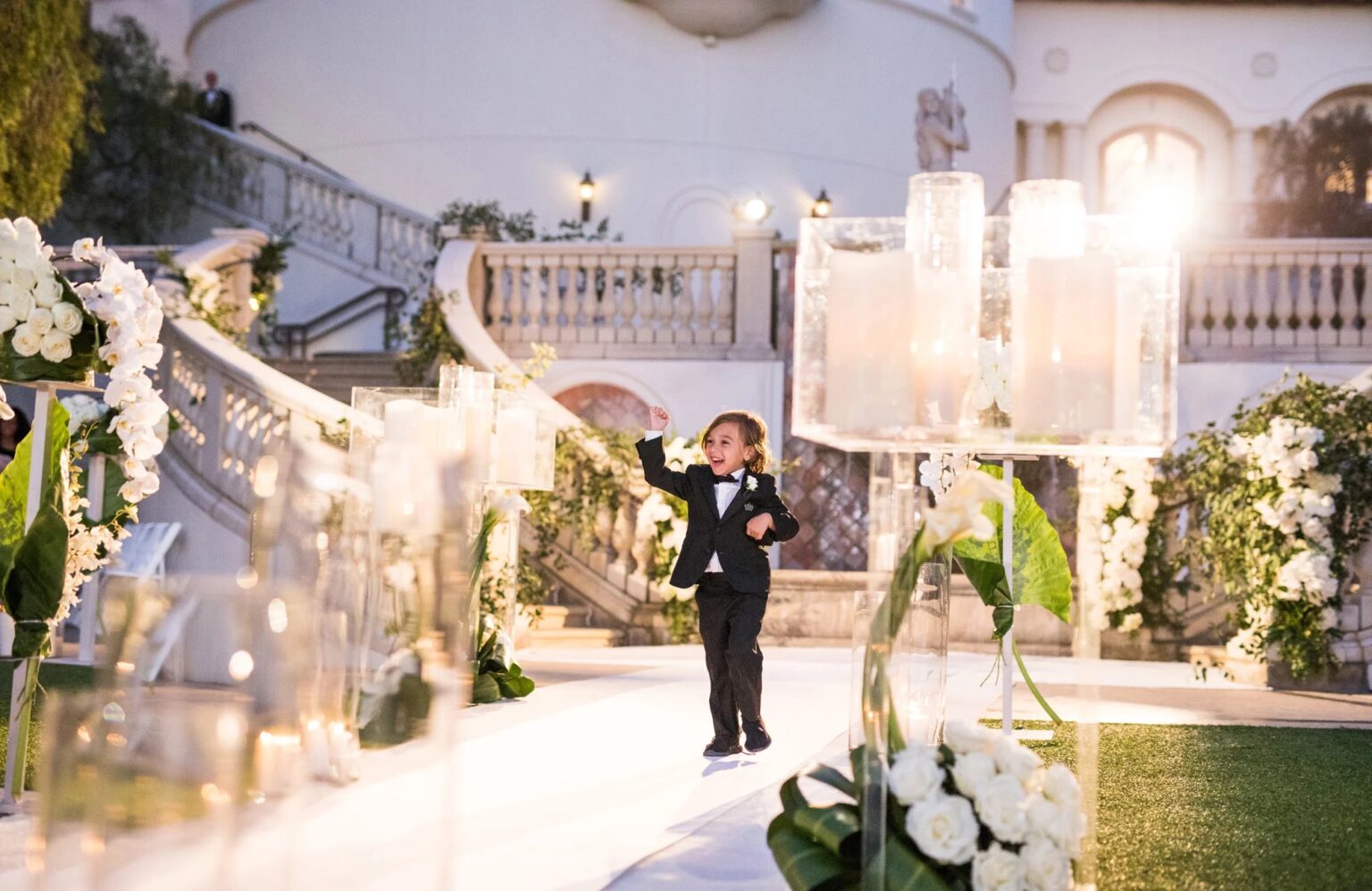 Candle blocks and white flowers along an outdoor aisle beside a stone terrace