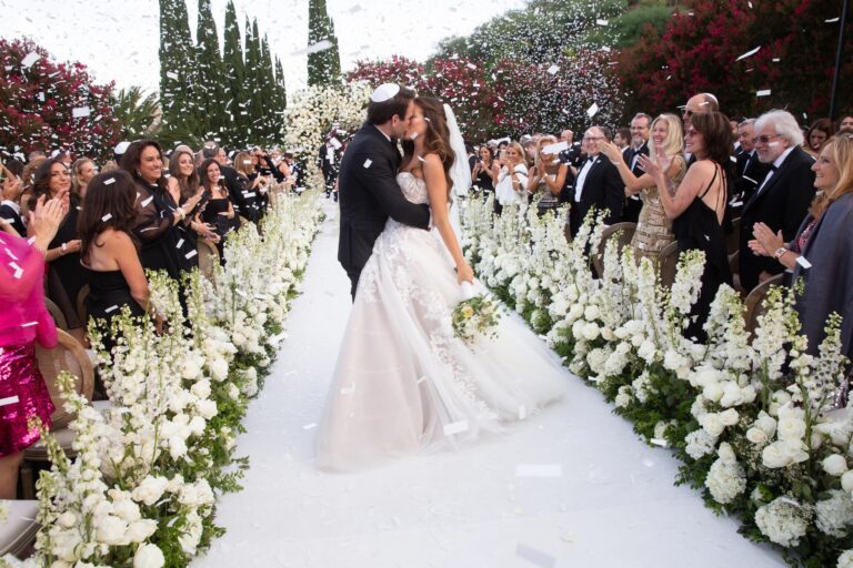 A couple kiss at the end of a white aisle lined with delphiniums as guests throw confetti, International Event Company