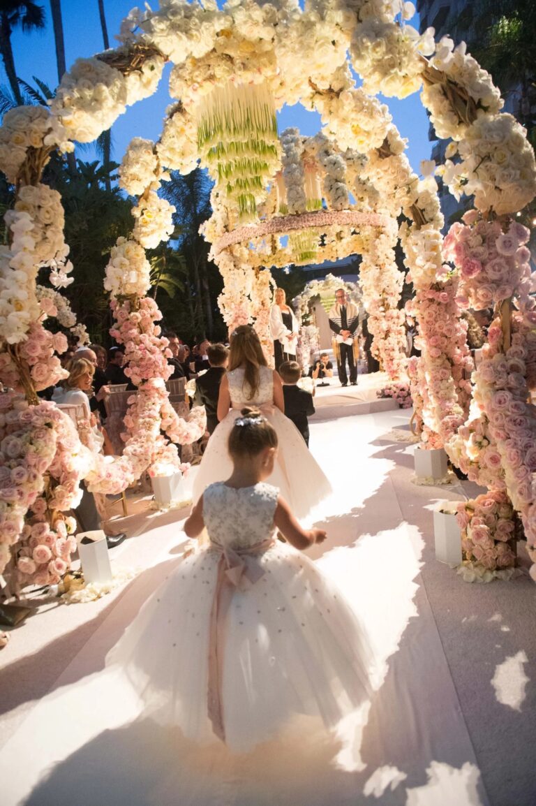 A flower girl walking beneath arches of white and blush roses with a hanging chandelier, International Event Company