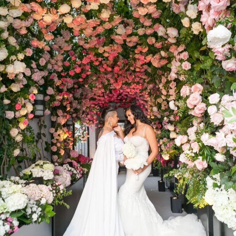Two brides beneath a pergola of pink and red roses, International Event Company