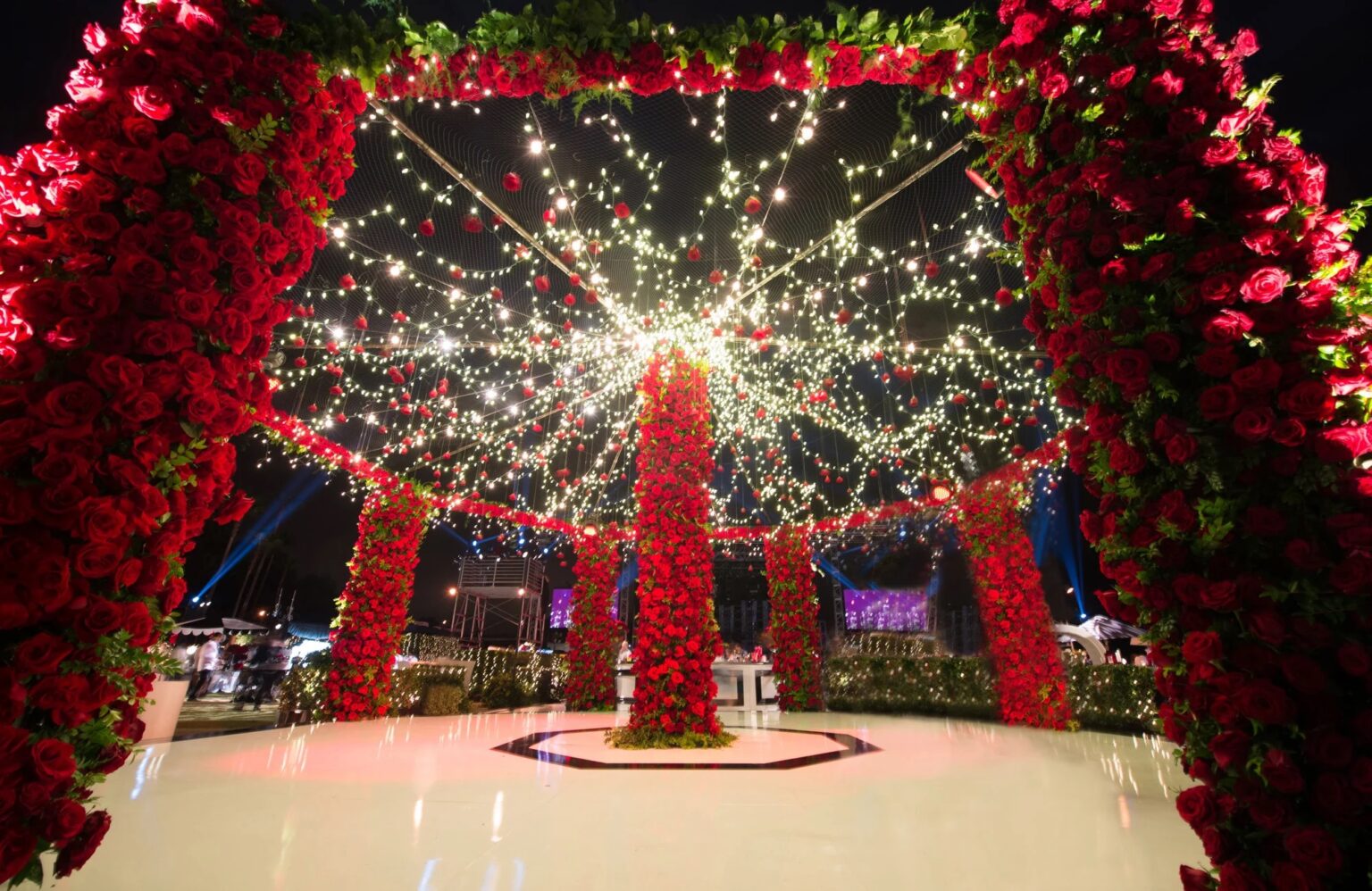 A red rose canopy hung with lights over a white dance floor at night