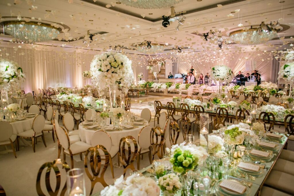A ballroom set with gold chairs, mirrored long tables and low white flowers