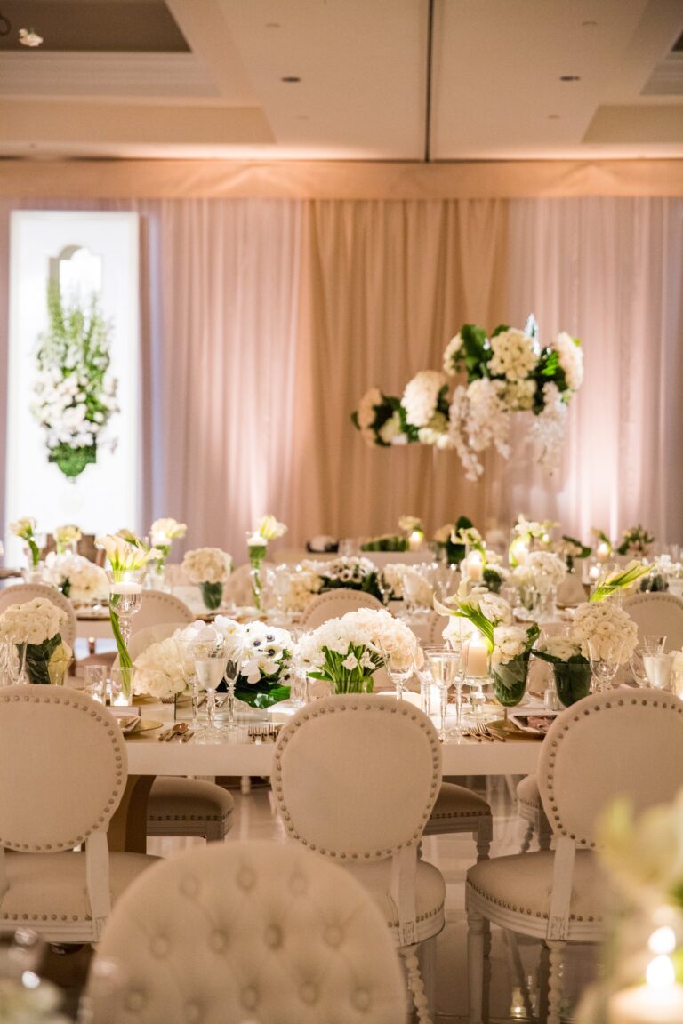 A white table with tufted chairs and tall floral arrangements in a ballroom, International Event Company