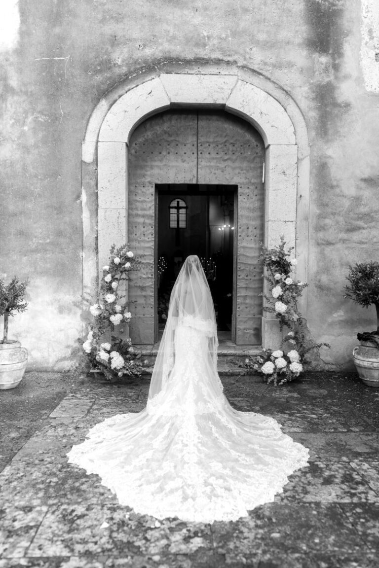 The bride at the church door, her train spread across the stone forecourt, Iole Criscitiello