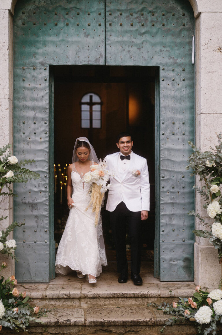 Newly married at the green church doors, flowers banked either side, Iole Criscitiello