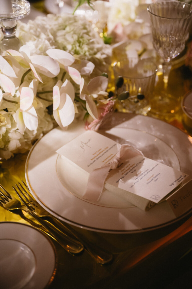 A place setting: gold charger, calligraphy menu and white orchids, Iole Criscitiello