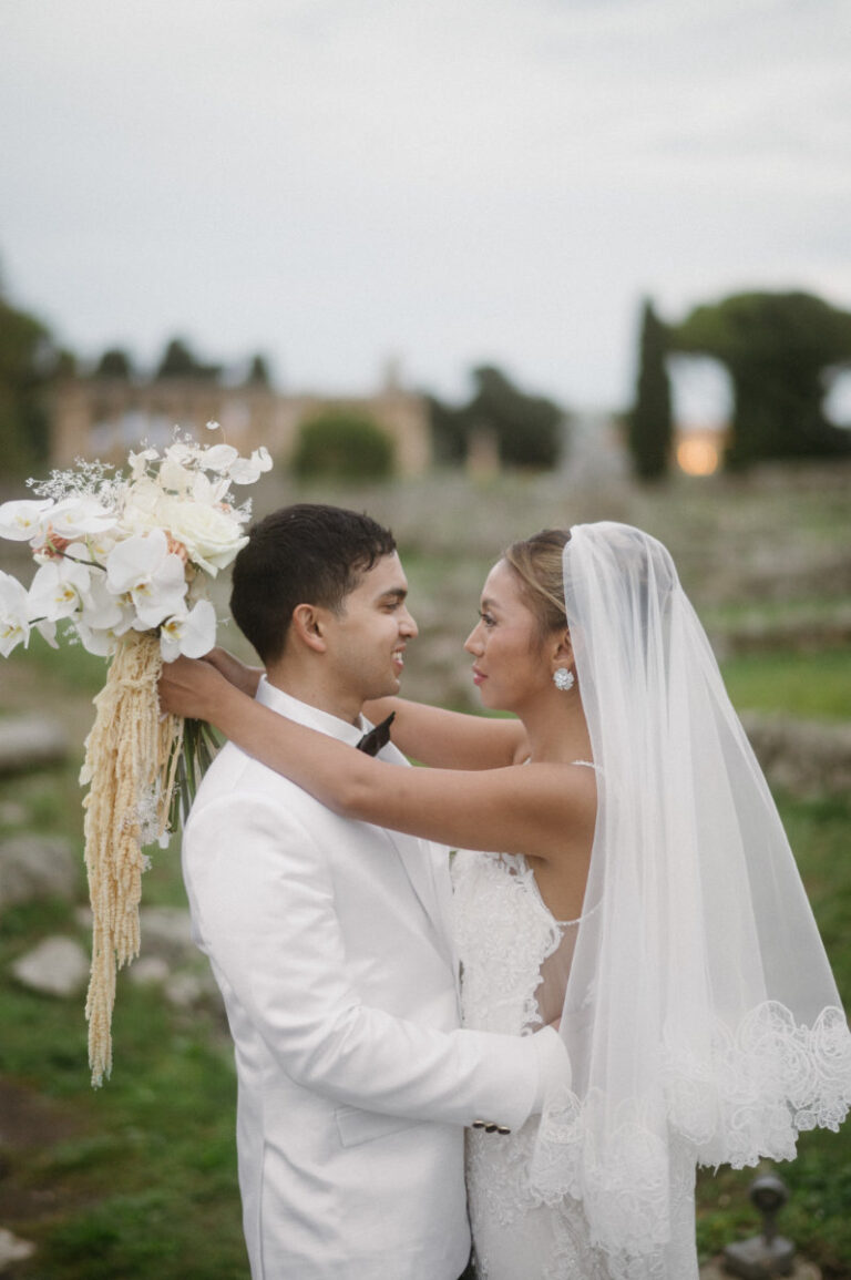 The couple among the ruins, a cascading white and amber bouquet in hand, Iole Criscitiello