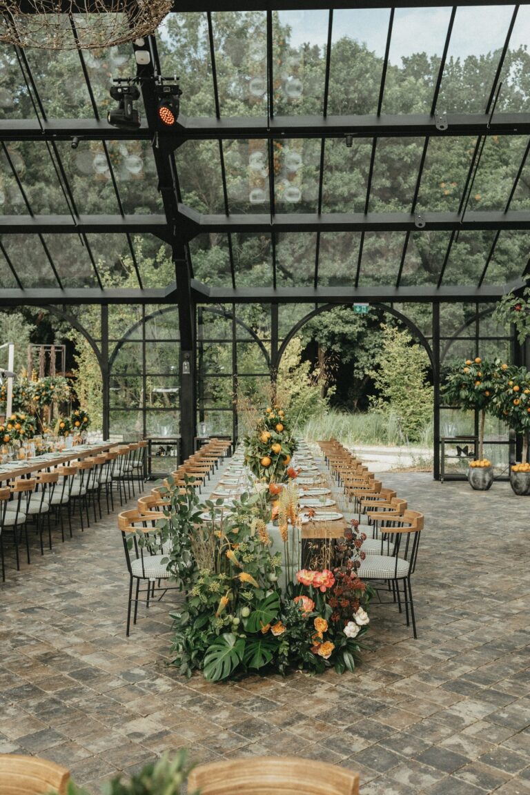 Long table with floral centrepieces inside the glasshouse, Iris Orangerie