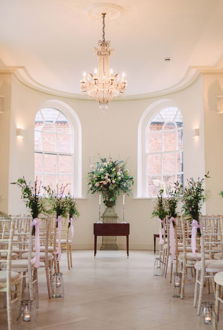 The Garden Room ceremony space, chandelier and arched windows above floral pedestals, Iscoyd Park