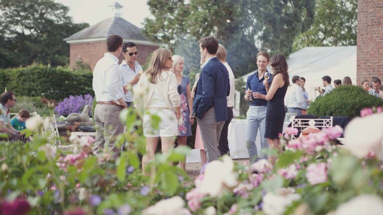 Guests with drinks among the flower borders of the gardens, a pavilion behind, Iscoyd Park