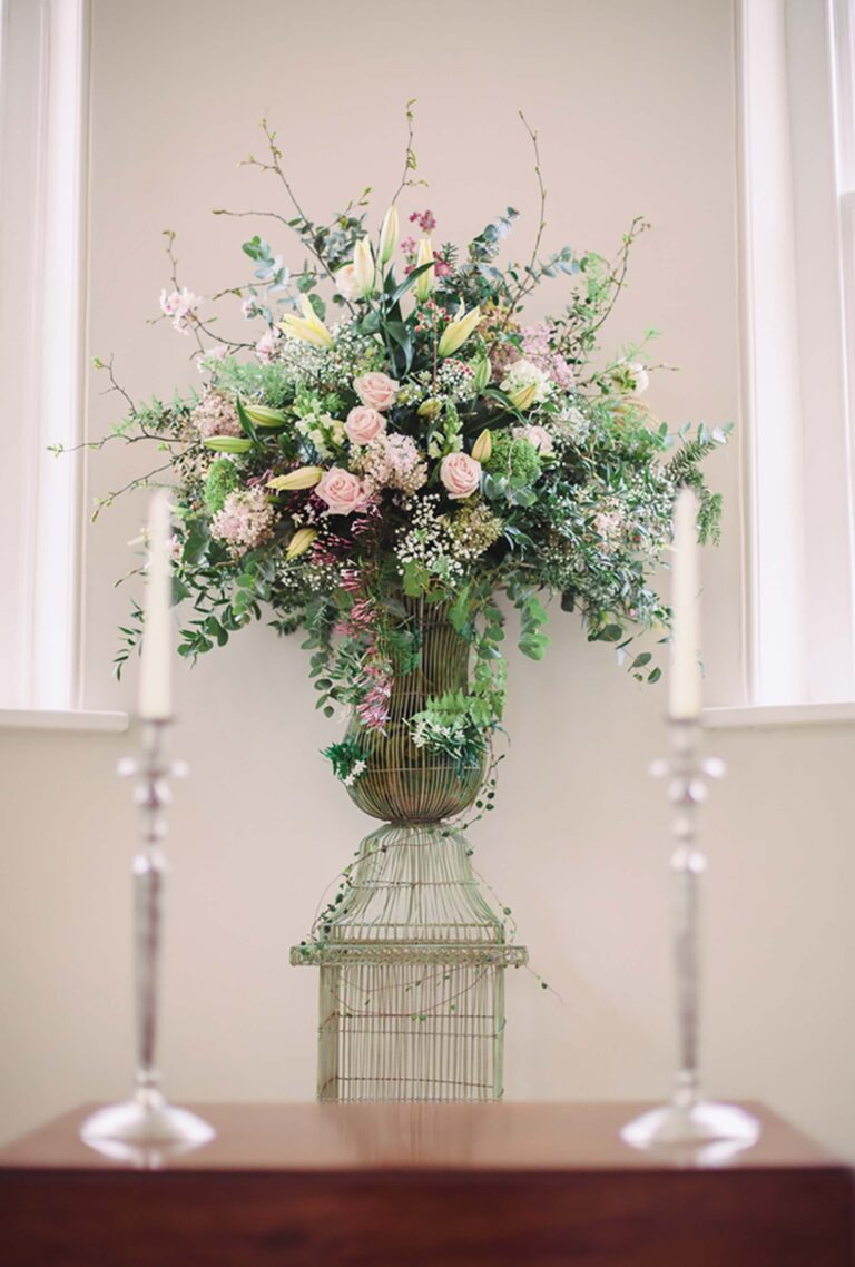 A tall pedestal arrangement of garden flowers between silver candlesticks, Iscoyd Park