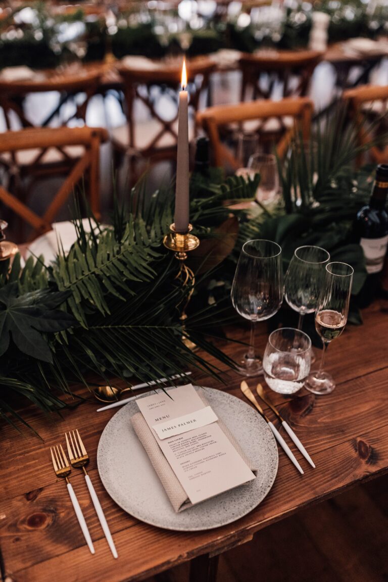 A place setting detail, a menu card, glassware and a trailing runner of greenery on a wooden table, Iscoyd Park