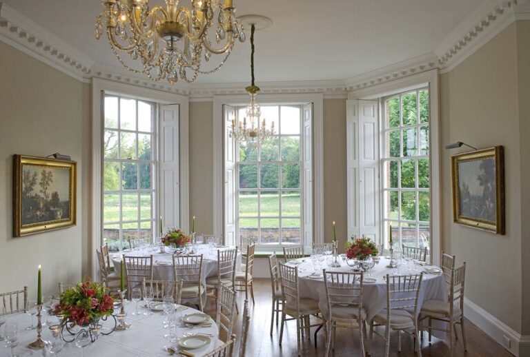 A bay-window drawing room set with round tables for a wedding breakfast, the garden beyond, Iscoyd Park