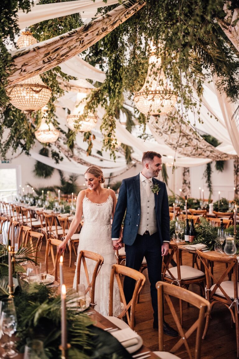 A couple in the Garden Room reception beneath a canopy of hanging foliage, long tables laid to either side, Iscoyd Park