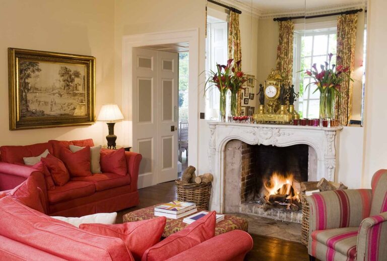 A cosy drawing room with a lit fire, a deep red sofa and oil paintings on the walls, Iscoyd Park