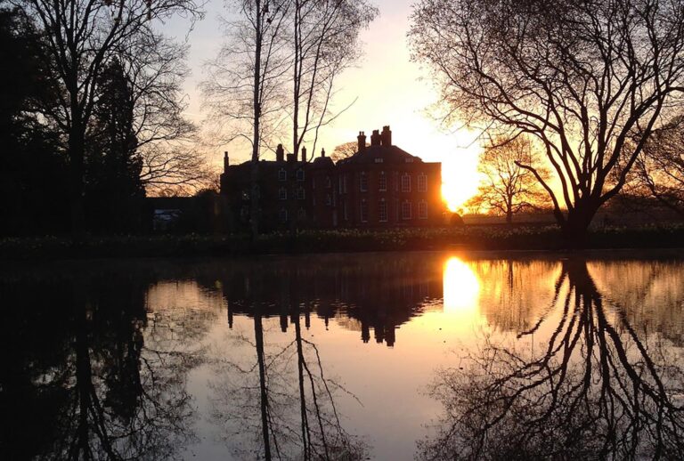The house in silhouette at sunset, mirrored in the still water below, Iscoyd Park