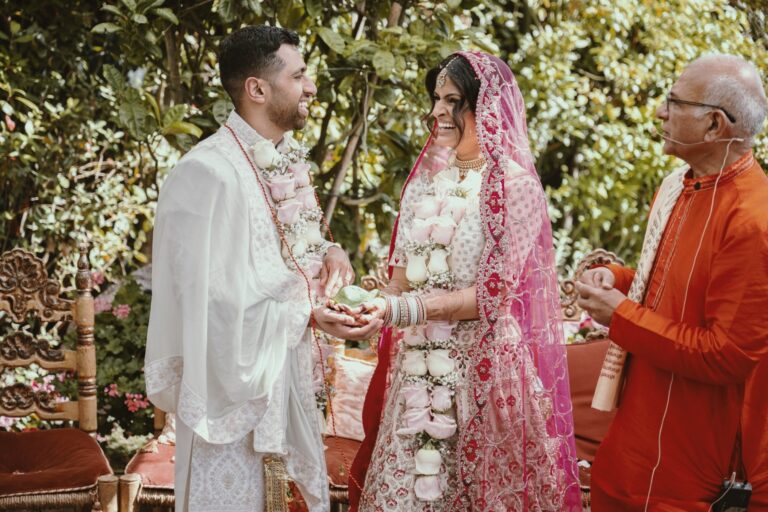 A Hindu ceremony under garden trees, groom and bride laughing mid-exchange, Italian Event Planners