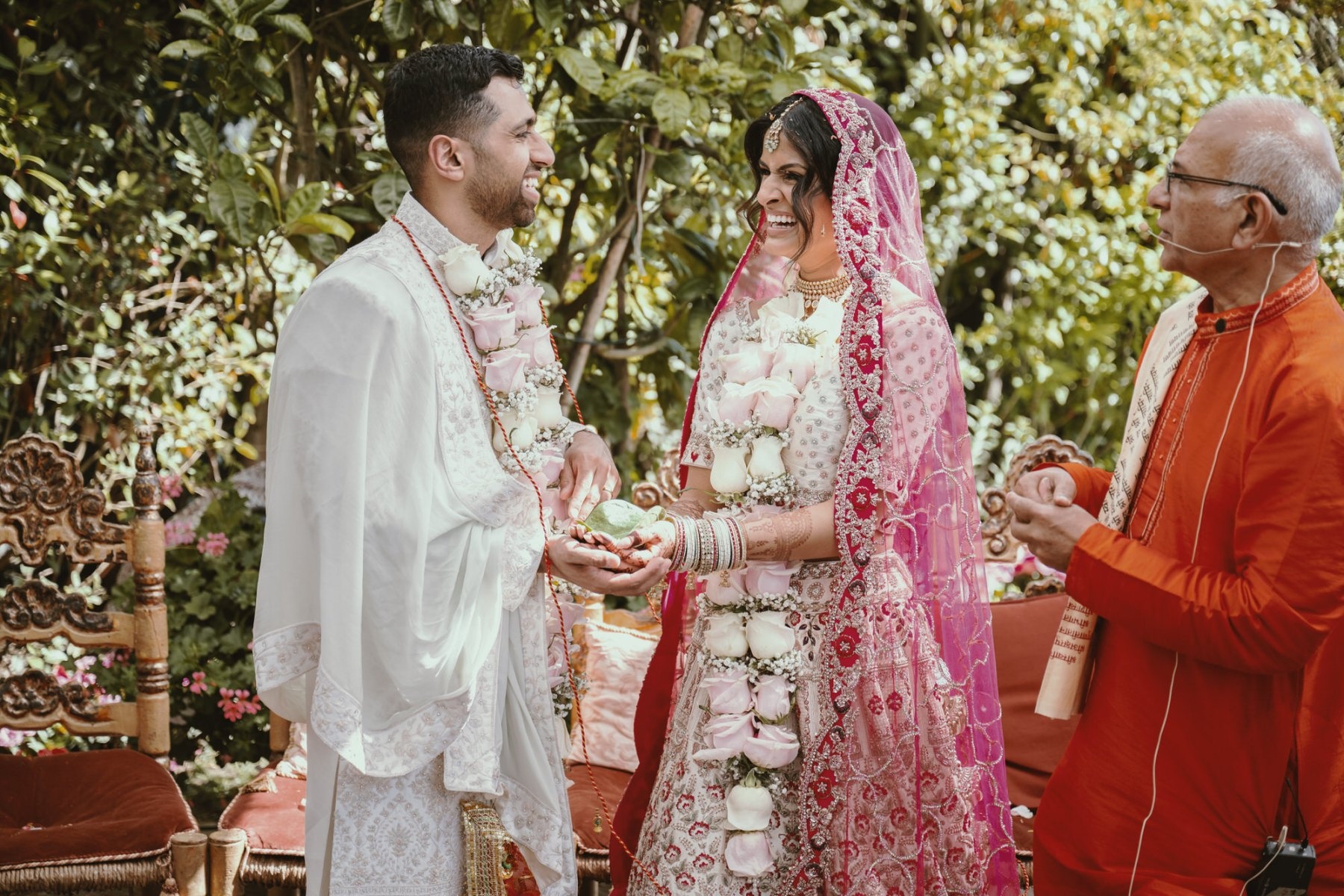 A Hindu ceremony under garden trees, groom and bride laughing mid-exchange, Italian Event Planners