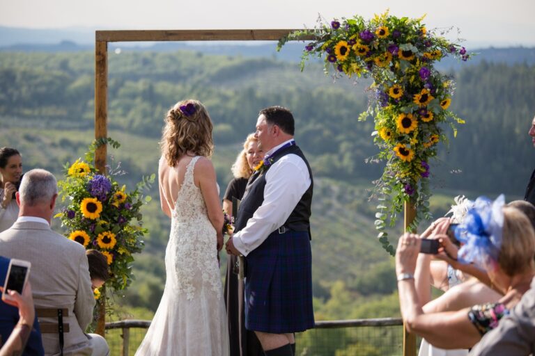 A couple at a sunflower-and-thistle arch overlooking Tuscan hills, the groom in a kilt, Italian Event Planners