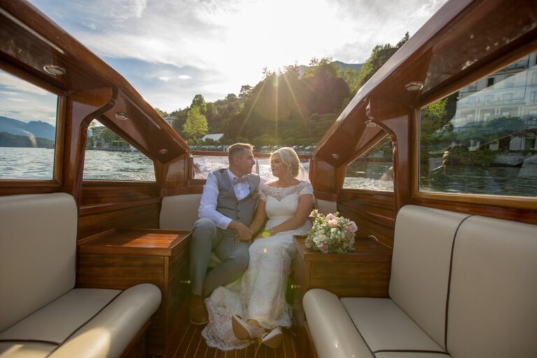 A couple seated in a varnished wooden boat on Lake Como, villas behind them, Italian Event Planners