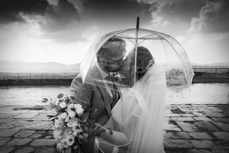 Black and white: a couple kissing under a clear umbrella in the rain on a hilltop terrace, Italian Event Planners
