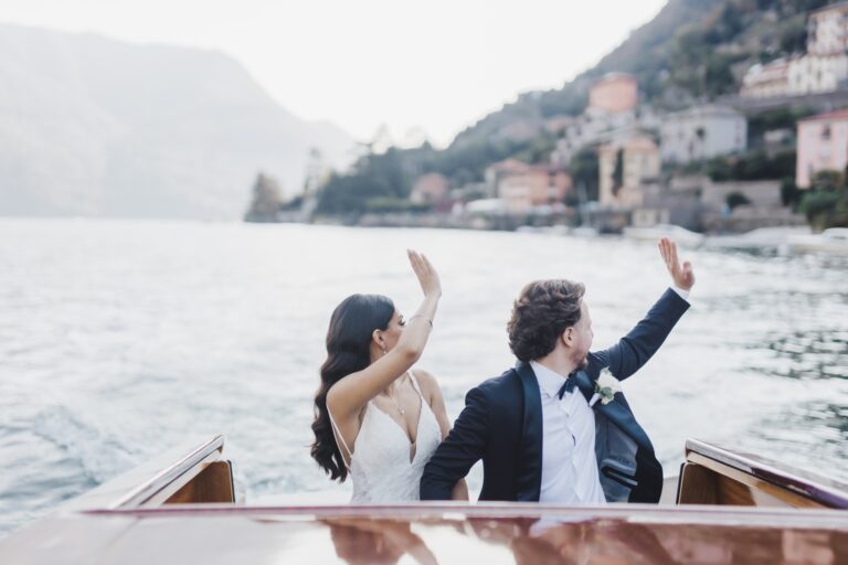 A couple waving from a departing boat, lakeside villas fading into the haze behind them, Italian Event Planners
