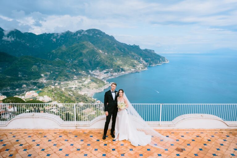 A couple on a clifftop balcony above Ravello, the Amalfi Coast spread out behind them, Italian Event Planners