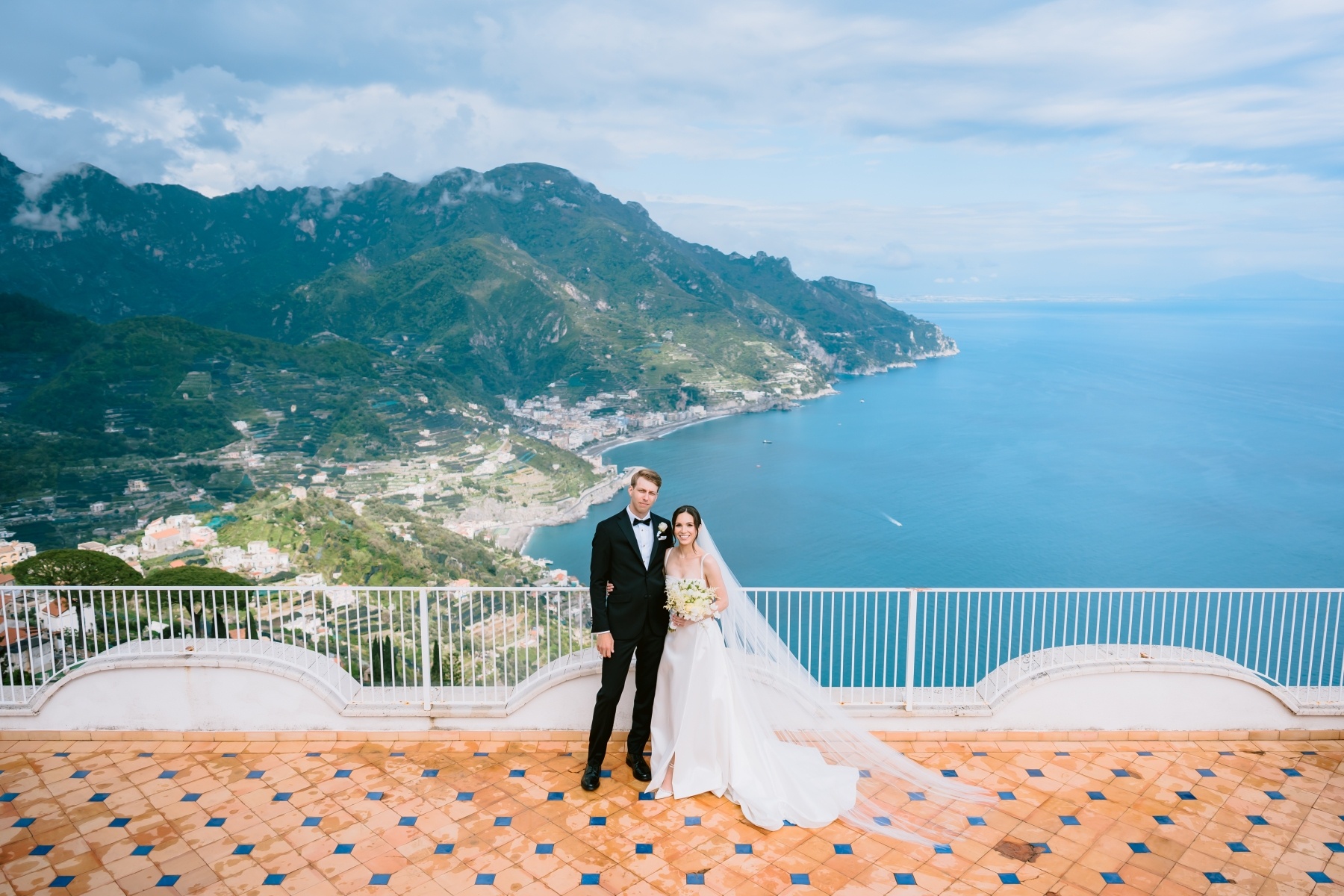 A couple on a clifftop balcony above Ravello, the Amalfi Coast spread out behind them, Italian Event Planners
