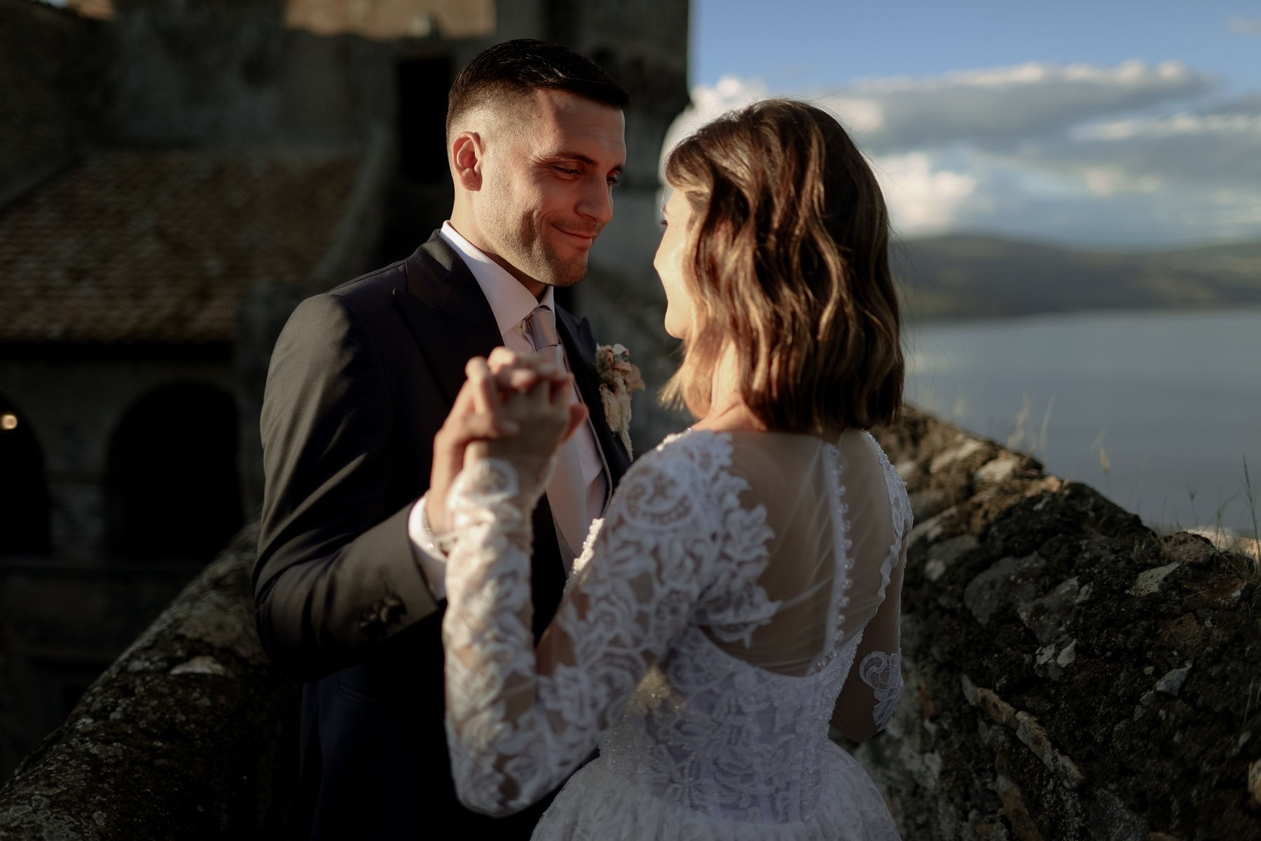 A couple dancing at golden hour beside a stone tower and a still lake, Italian Event Planners
