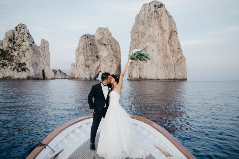 A couple kissing on the bow of a boat before Capri's Faraglioni sea stacks, Italian Event Planners