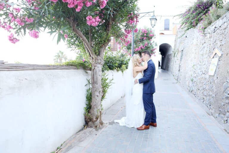 A couple kissing under a bougainvillea-covered tree in a narrow Amalfi Coast lane, Italian Event Planners