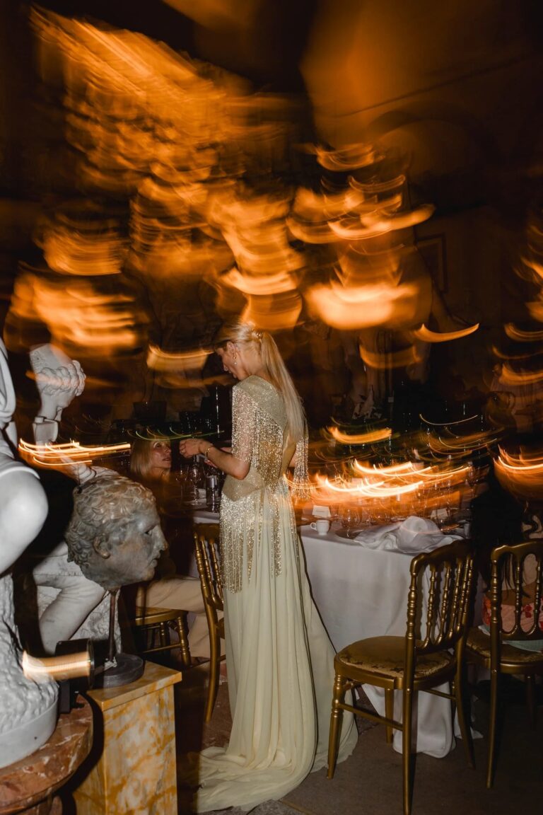 A reception in a Florentine sculpture gallery, a guest in a beaded gown caught in the candle light among marble busts, Italian Eye