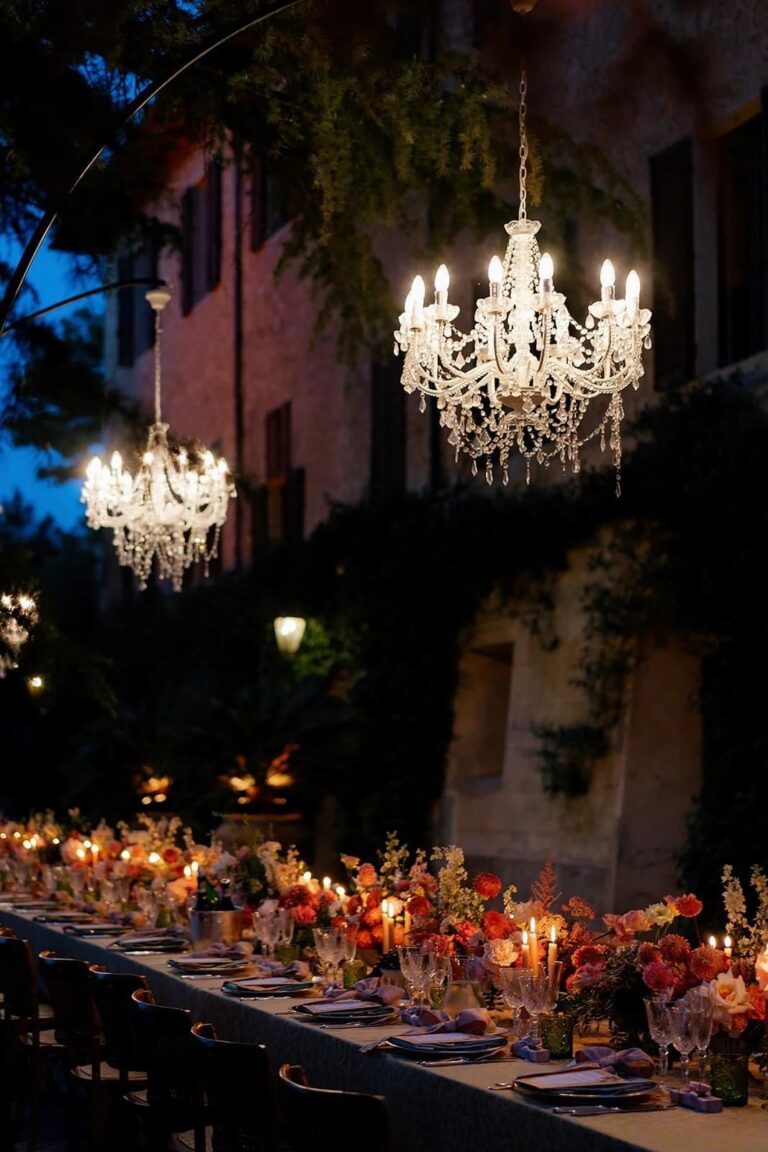 A long table of autumn flowers under crystal chandeliers outside a Tuscan villa at dusk, Italian Eye
