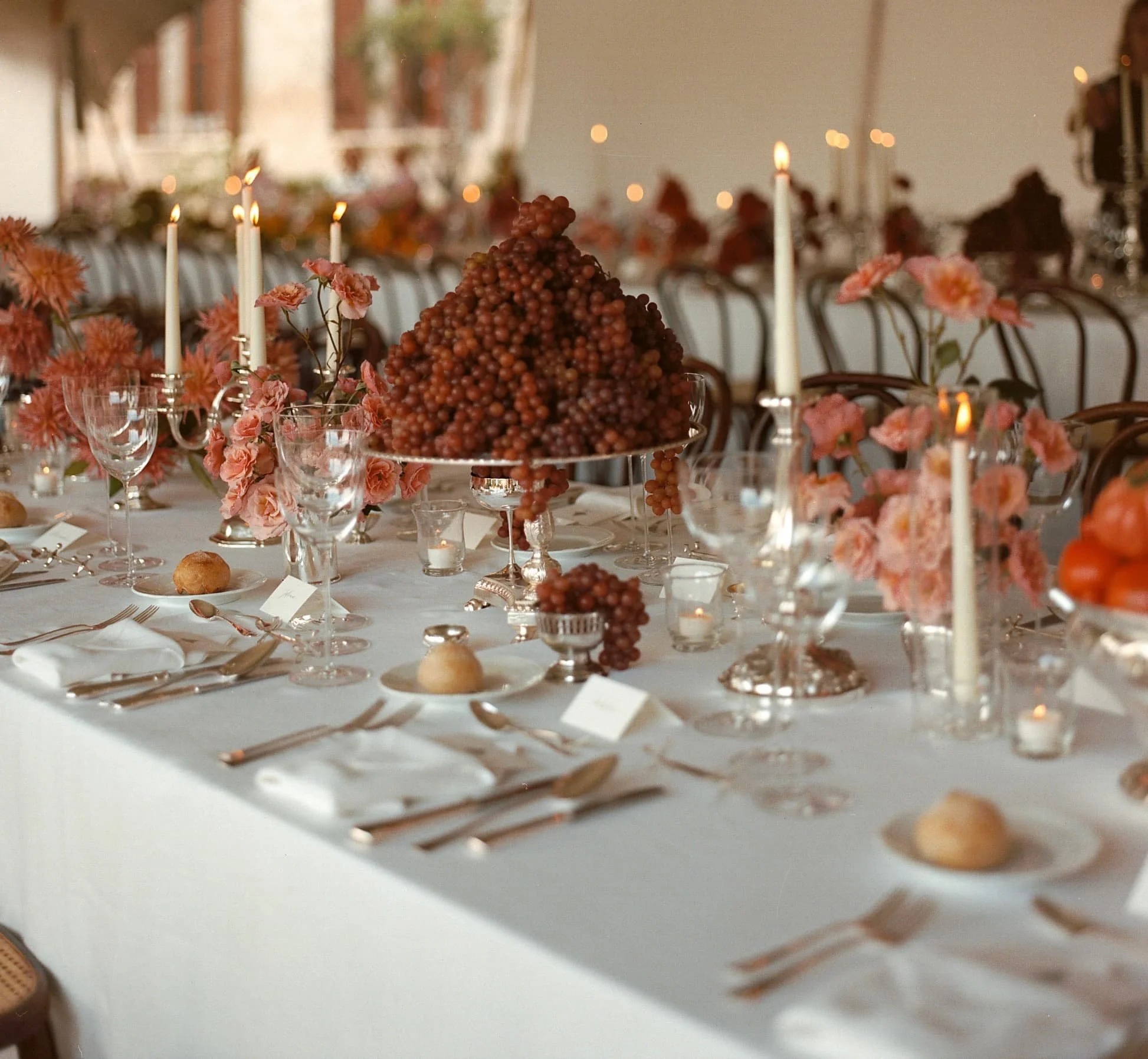 A marquee reception table with a pyramid of red grapes, coral dahlias and ivory tapers, Italian Eye