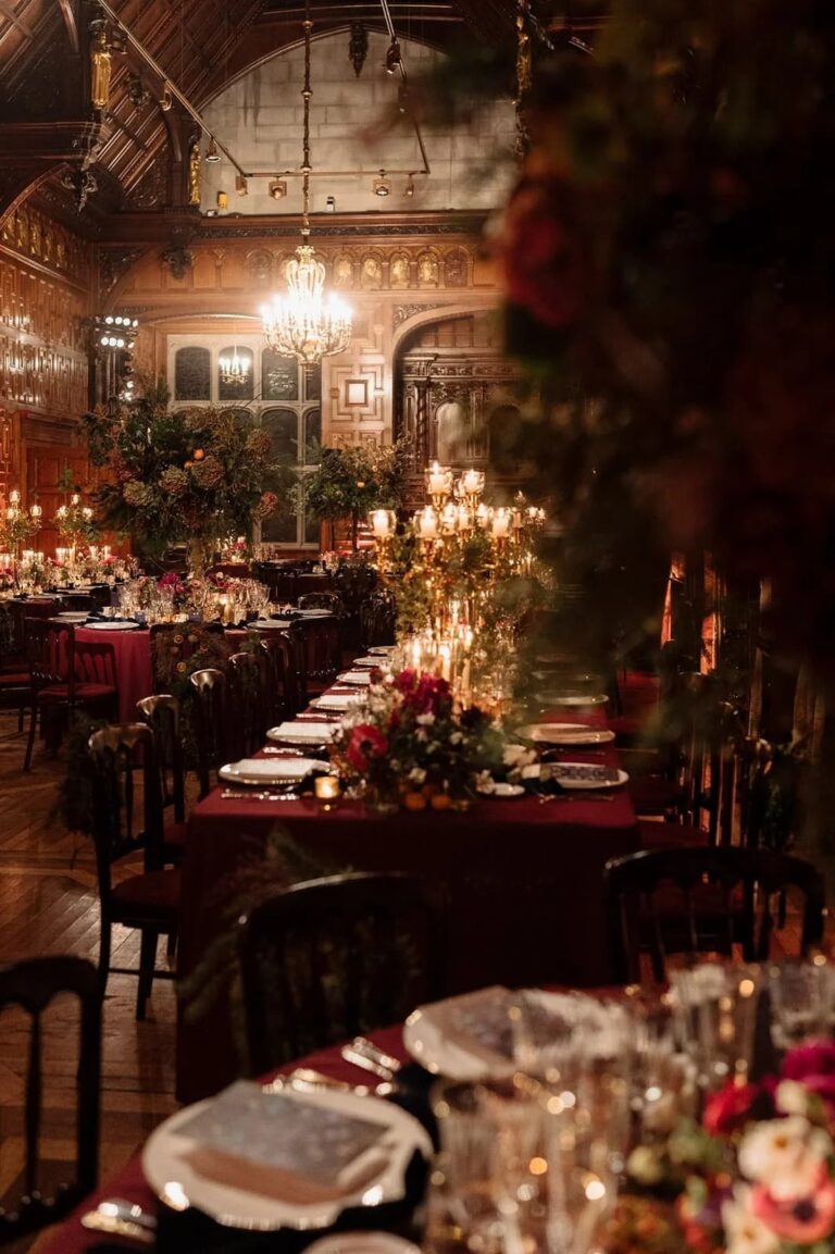A timber-vaulted great hall set for dinner with burgundy linen and gilt candelabra, Italian Eye