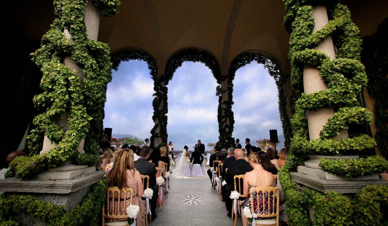 A ceremony in the ivy-covered loggia at Villa del Balbianello, Lake Como, the lake framed by the arches, Italian Wedding Company