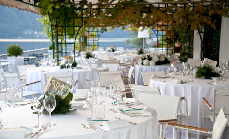 Round tables laid in white under a vine pergola open to Lake Orta at Hotel Giardinetto, Italian Wedding Company